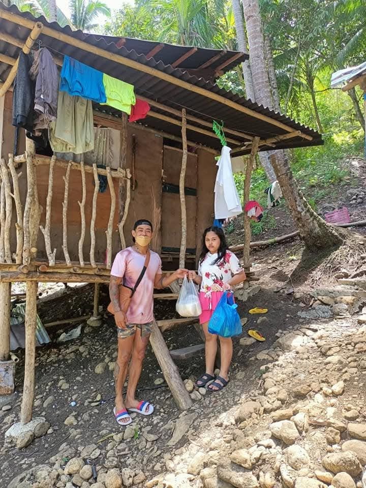 A volunteer handing a food package to a woman outside a home