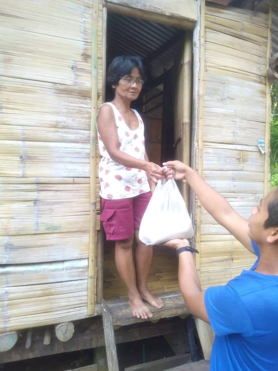 A volunteer handing a food bag to a woman in a doorway